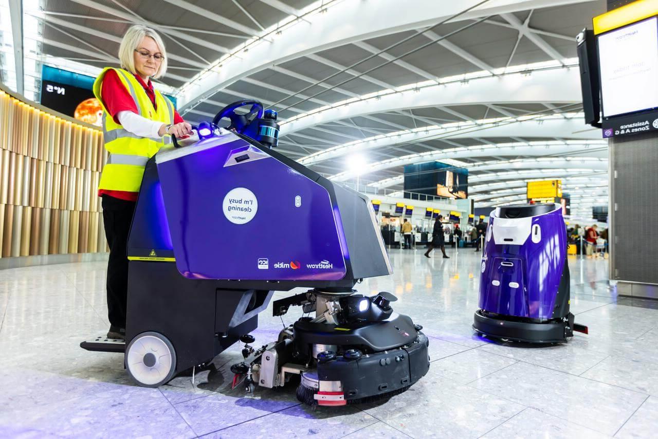两个紫色的清洁机器人, 和一个清洁同事, 在伦敦希思罗机场候机楼